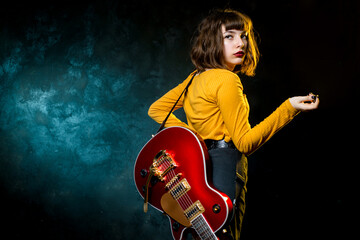Trendy young hipster woman with curly hair with red guitar in neon lights. Rock musician posing with electrical guitar.