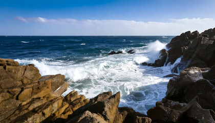 Obraz premium Dramatic ocean waves crashing against rugged coastal rocks under a vibrant blue sky. Perfect for travel, nature, and environmental projects.