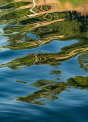 A small sailboat floats on a calm river Nile, its reflection distorted by gentle ripples creating an abstract pattern on the water's surface.
