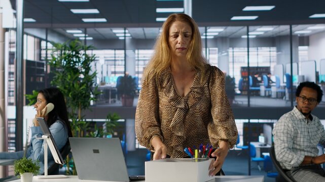 Distraught employee losing her job and collecting her belongings, leaving her office and feeling worried about unemployment. Woman getting fired after a conflict, dismissed. Camera A.