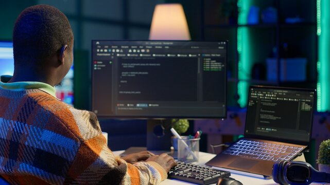 Black software engineer writes complex binary code scripts on computer, cybersecurity. Teleworking IT specialist in home office using programming language to safeguard consumer data. Camera A.