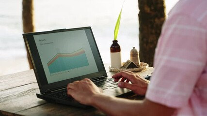 Freelancer analyzes business progress on laptop at oceanfront cafe. Sunset seascape, work-life balance. Man examines growth charts, strategy planning by sea. Remote job, data analysis during travel - Powered by Adobe