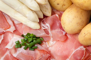 A setting of fresh white asparagus, potatoes and gammon decorated with cut chives.  Studio shot.
