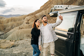 Couple taking selfie in desert by camper van during road trip