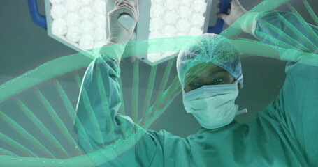 Image of dna strand rotating over african american female surgeon working in theatre