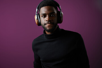Young Black man in stylish headphones enjoying music against a purple background, showcasing a modern lifestyle and vibe
