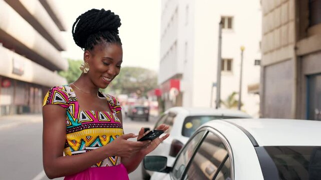 Smiling African woman using phone outdoors, bright African print dress.