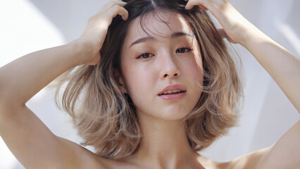 Fototapeta premium 軽く膝の上に手を置き、柔らかく自然なポーズで座っているセミロングの若い日本人女性、穏やかで優雅な表情、輝くような肌