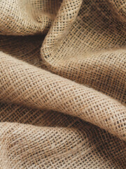 A beige jute fabric texture with a natural, woven appearance. The fibers are slightly irregular and textured, showcasing the organic and rustic feel of burlap