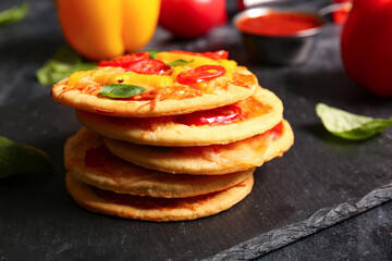 Board with tasty mini pizzas on black background