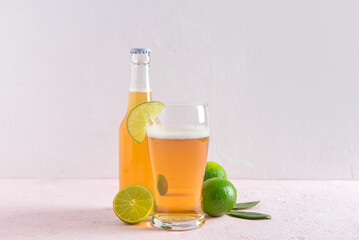 Glass and bottle of cold beer with lime on light background