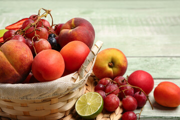 Wicker basket with different fresh fruits on green wooden background, closeup
