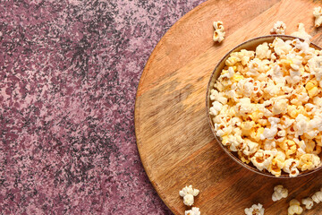 Bowl with tasty popcorn on purple background