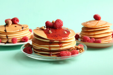 Plates of tasty pancakes with raspberries and nuts on turquoise background