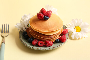 Plate of tasty pancakes with raspberries and blueberries on yellow background