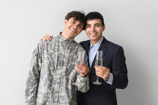 Young soldier with his husband and champagne on light background