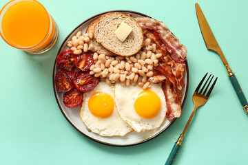 Plate with tasty English breakfast and glass of juice on turquoise background