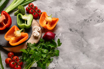 Boards with fresh vegetables and greenery on grunge grey background