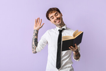 Happy young man in shirt reading book on lilac background