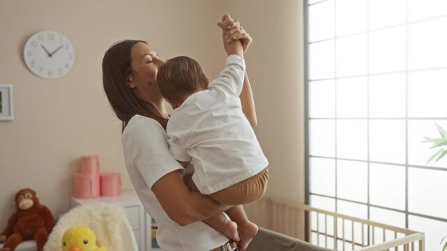 Woman dancing joyfully with her son in a bright bedroom, surrounded by soft toys and furniture, creating a warm and loving atmosphere indoors.