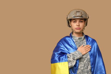 Young female soldier in uniform with flag of Ukraine on beige background