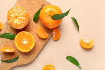 Wooden board with sweet mandarins and leaves on beige background