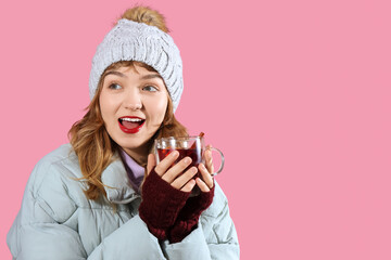 Smiling young woman in winter clothes with mulled wine on pink background, closeup
