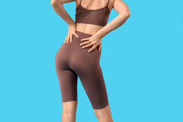 Young woman in cycling shorts on blue background, back view