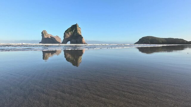 Wharariki Beach. Waves rolling over reflection of the islands. West Coast of the South Island, New Zealand