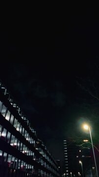 Nighttime shot of an office building with illuminated windows and a nearby streetlamp casting a soft glow, highlighting the modern urban environment. Amsterdam, Nederland.