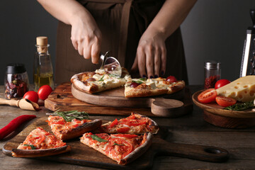 Woman cutting tasty pizza on wooden table
