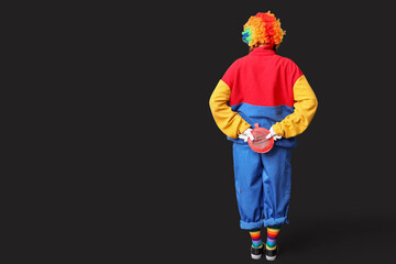 Fototapeta premium Young woman dressed as sad clown with whoopee cushion on black background, back view. April Fool's day celebration