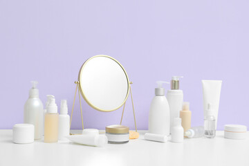 Different cosmetic products with mirror on table near lilac background