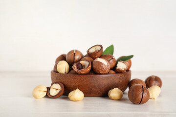 Bowl with tasty macadamia nuts on white wooden background