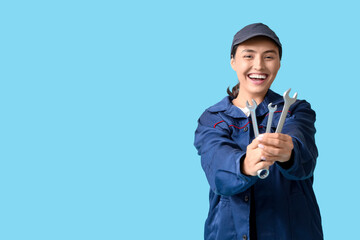 Young female mechanic with wrenches on blue background. Woman in male profession concept