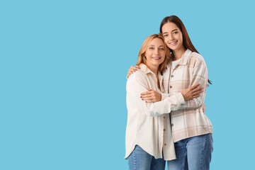 Fototapeta premium Pretty young woman hugging her mother on blue background. International Hug Day