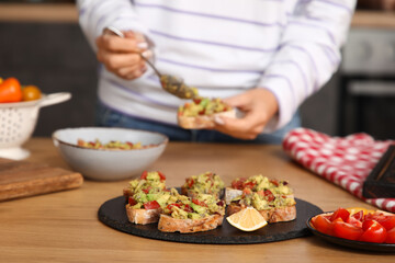 Tasty vegan bruschettas on table against woman cooking in kitchen, closeup