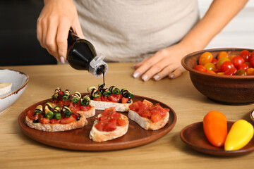Young woman pouring sauce onto vegan bruschettas at table in kitchen, closeup