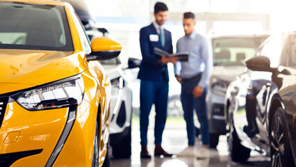 Customer middle eastern guy standing among brand new cars, having conversation with male sales...