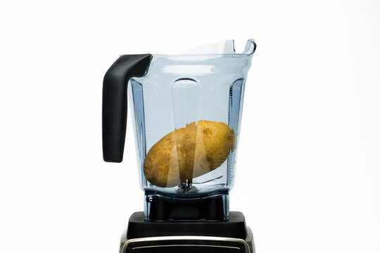 A whole russet potato in a clear plastic blender against a white backdrop