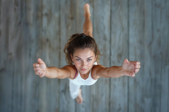 Woman performing yoga warrior crescent lunge pose with precision and strength, captured from above on rustic wooden floor