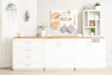 Interior of light kitchen with white counters and folding screen near white wall, blurred view