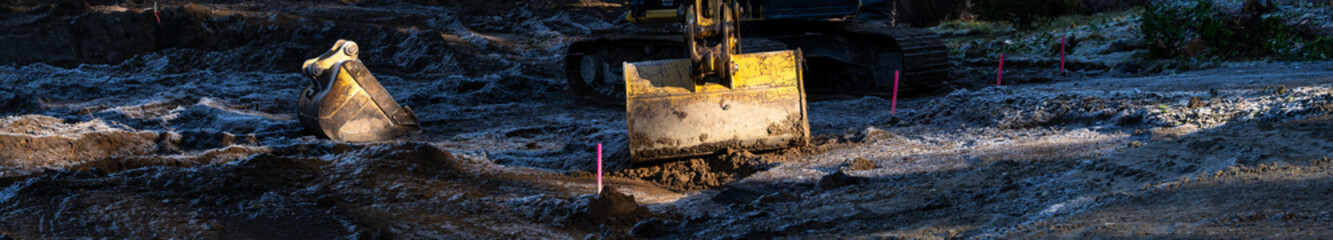 Excavation heavy equipment on a cleared residential house lot for construction of new home, frozen and frost covered dirt with surveyor stakes
