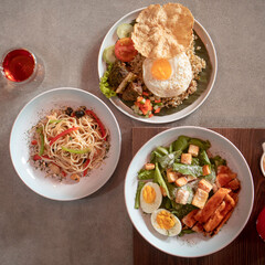 Succulent dishes include fried rice topped with an egg, flavorful noodles with vegetables, and a fresh mixed salad, enjoyed at midday