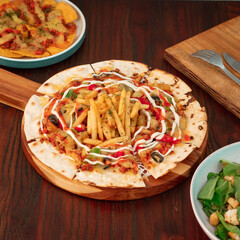 A loaded flatbread features crispy fries, fresh veggies, and a drizzle of dressing alongside refreshing salad and cheesy nachos