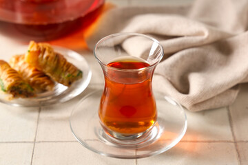 Glass of Turkish tea with tasty baklava on white tile background