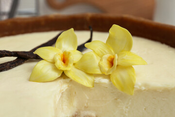 Cut sweet cheesecake with vanilla flowers and sticks, closeup