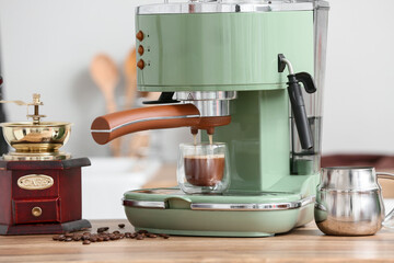 Modern coffee machine with glass of hot espresso and beans on wooden table in kitchen