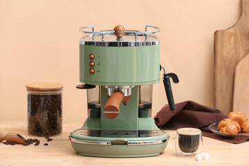 Modern coffee machine with glass of hot espresso and sweet cakes on beige background