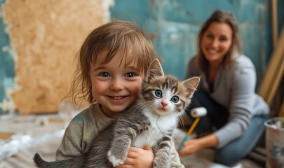 Obraz premium A child joyfully holds a playful kitten, smiling brightly. Behind them, a parent is working on home improvement tasks, creating a warm and lively atmosphere indoors